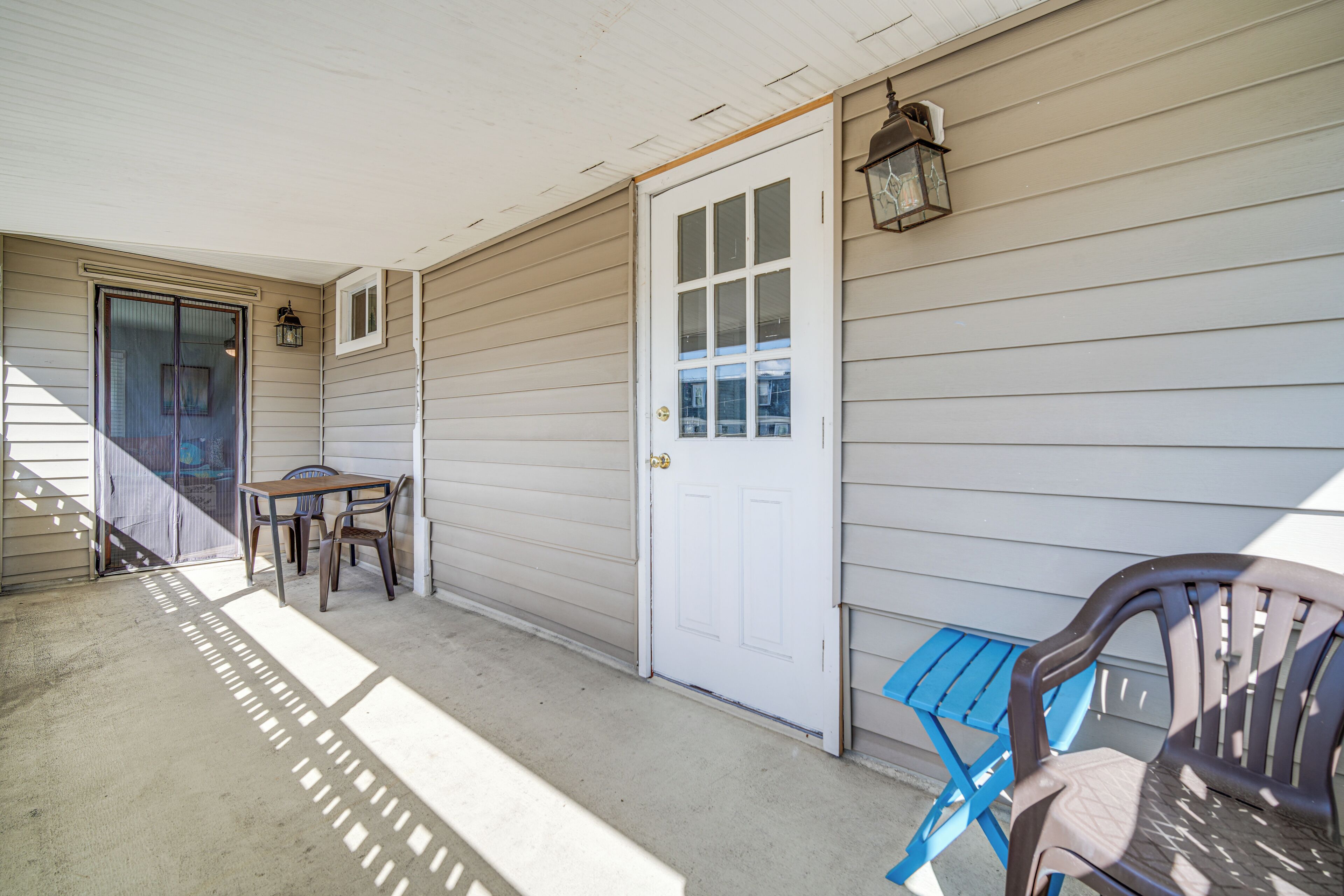 A covered porch with a door, a table, and two chairs.
