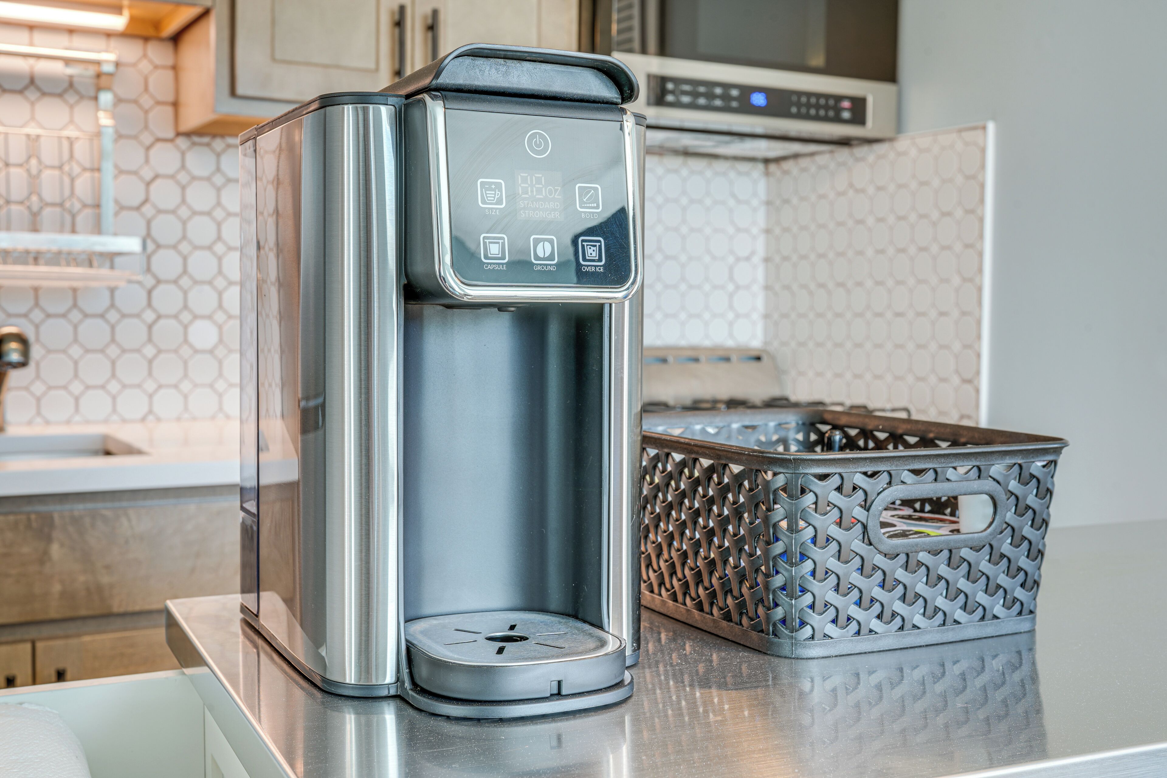 A modern coffee maker with a digital interface, a stainless steel basket, and a kitchen counter.