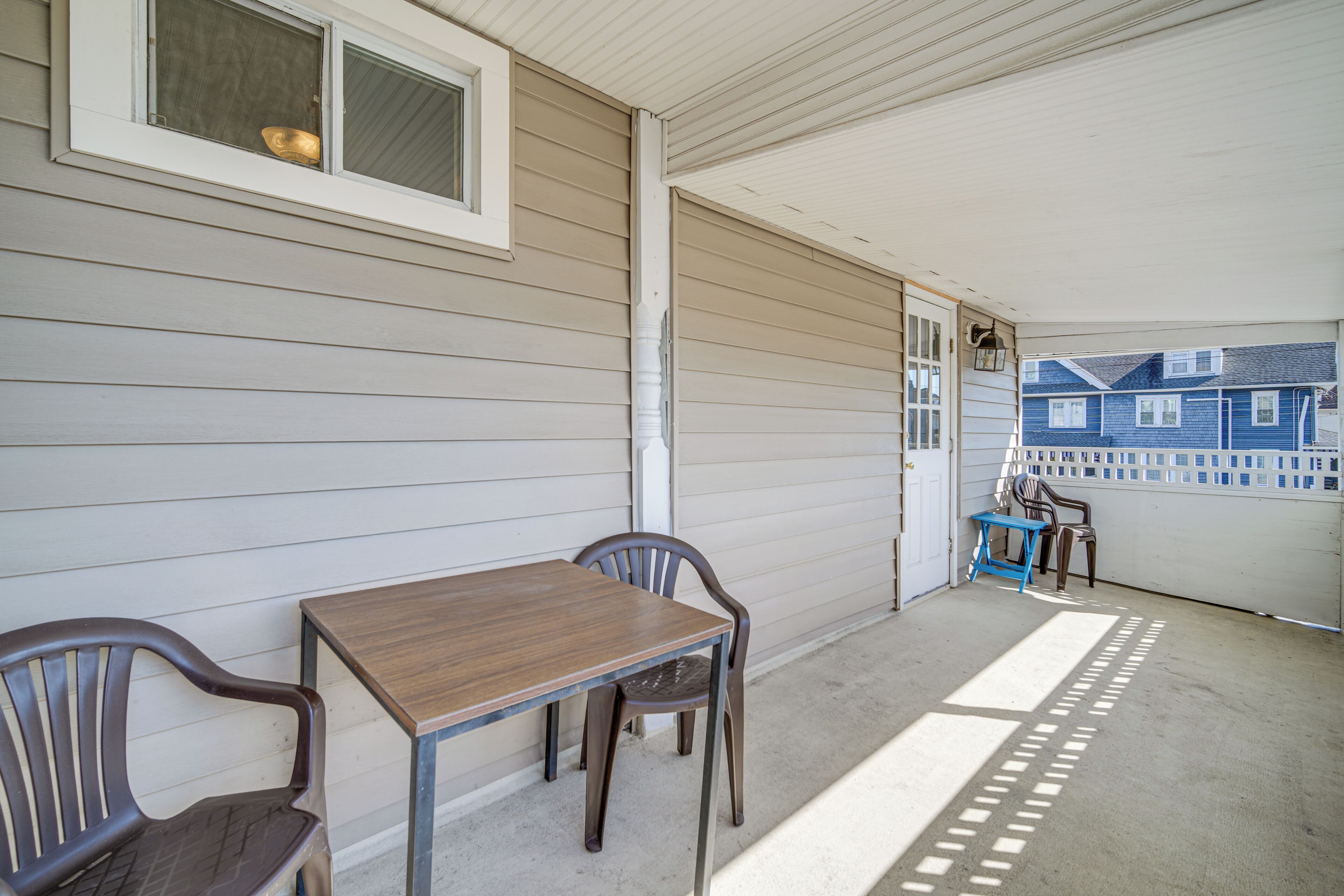A covered porch with a table and chairs, a window, and a view of neighboring houses.