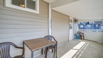 A covered porch with a table and chairs, a window, and a view of neighboring houses.