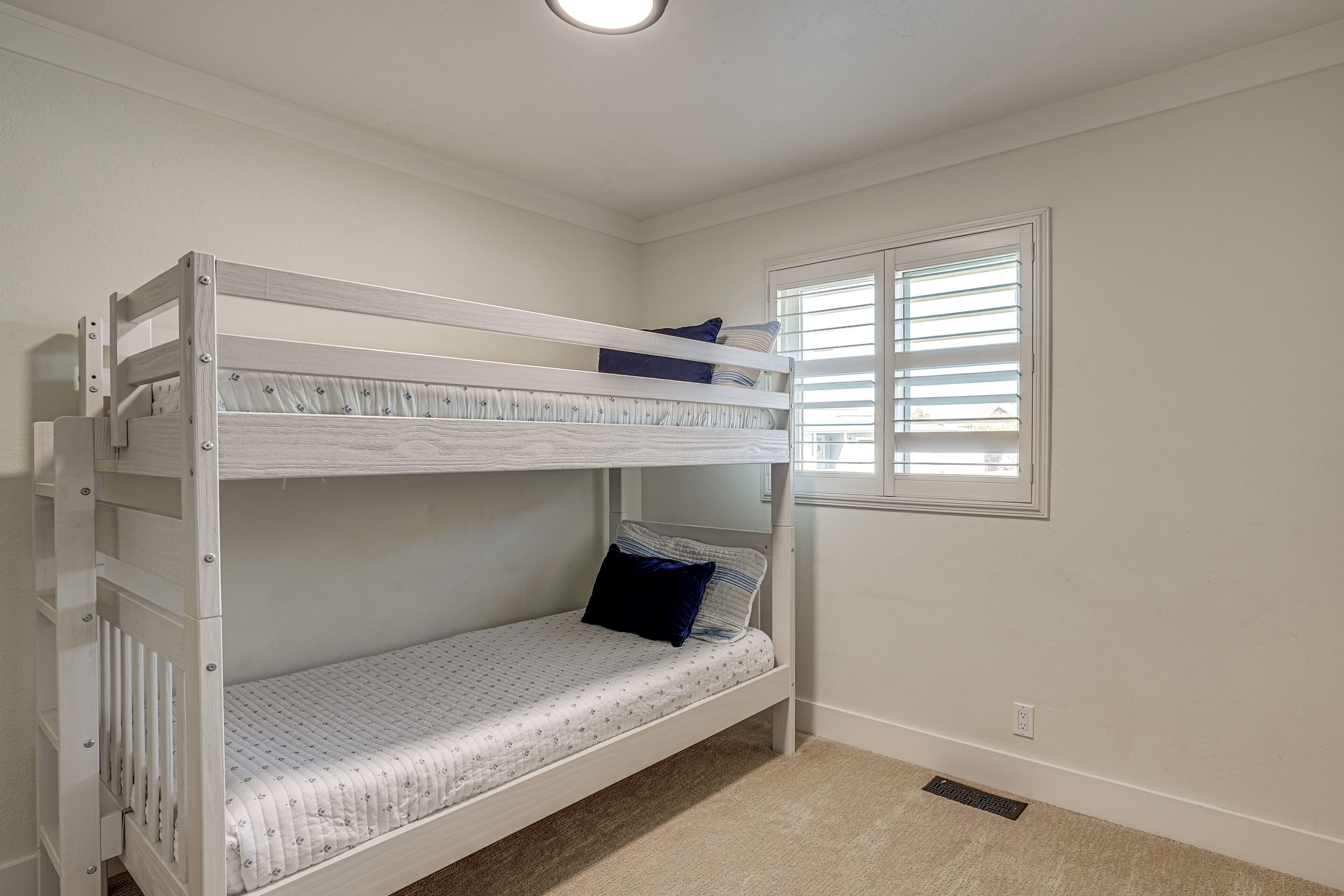 A bunk bed in a room with a window and a power outlet on the wall.