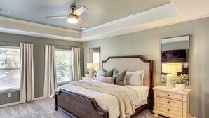 A bedroom with a large bed, bedside tables, a ceiling fan, and a window with curtains. - Golf, Shop + Relax: Family Bluffton Home (Bluffton)