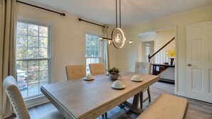 Una sala da pranzo con un tavolo in legno, quattro sedie, un lampadario e vista all'esterno attraverso ampie finestre.