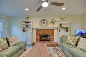 A living room with two green sofas, a wooden coffee table, a brick fireplace, white shelving units, and a ceiling fan. - Fully Updated! Suburb Stay Near Sugarloaf Mills (Lawrenceville)