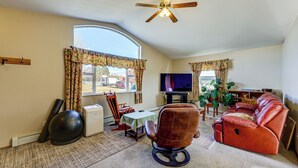 Ein Wohnzimmer mit Deckenventilator, Fernseher, einem roten Ledersofa, einem braunen Ledersessel, einem kleinen Tisch und einem großen Fitnessball.