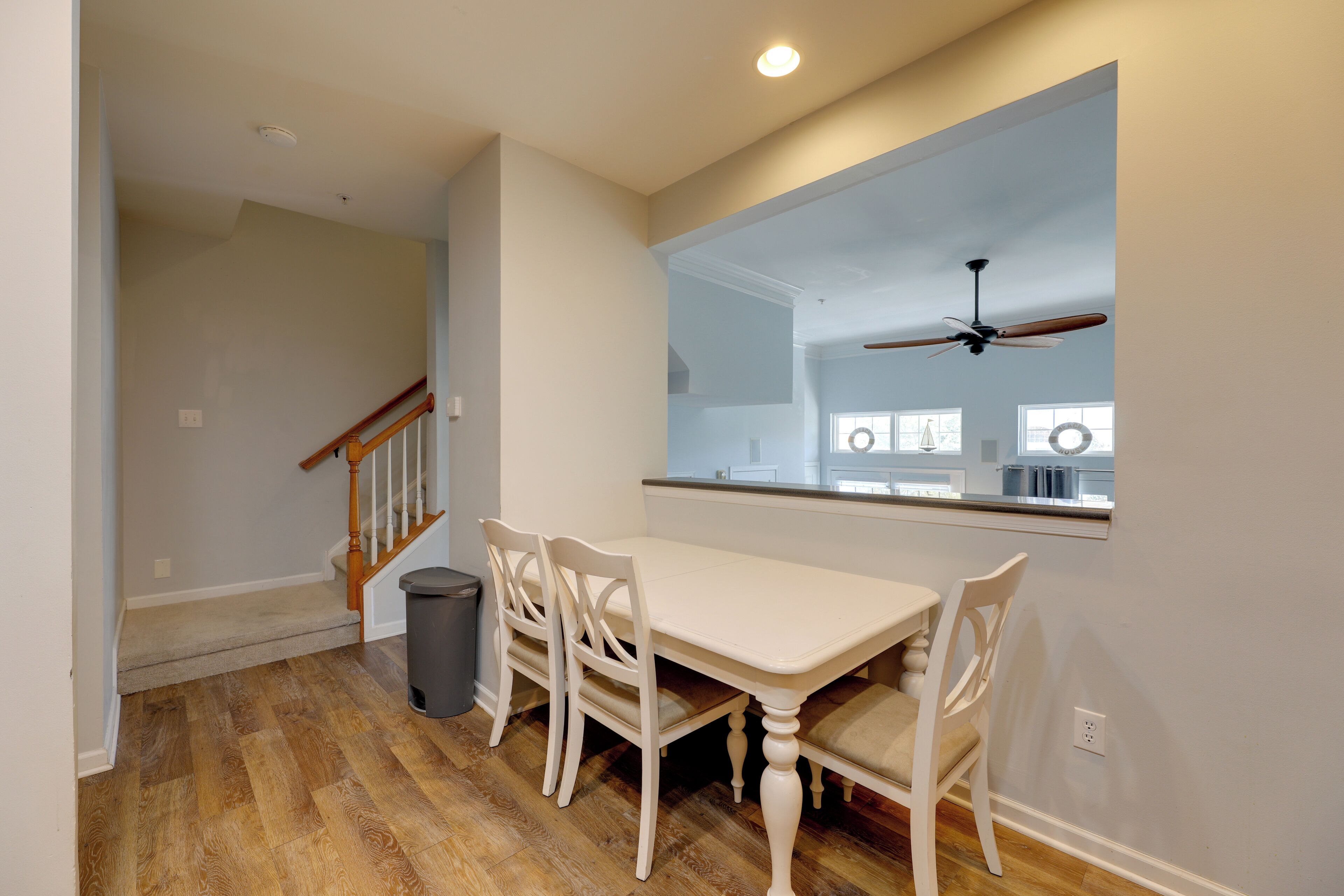 A dining area with a white table and chairs, a wooden floor, and a ceiling fan.