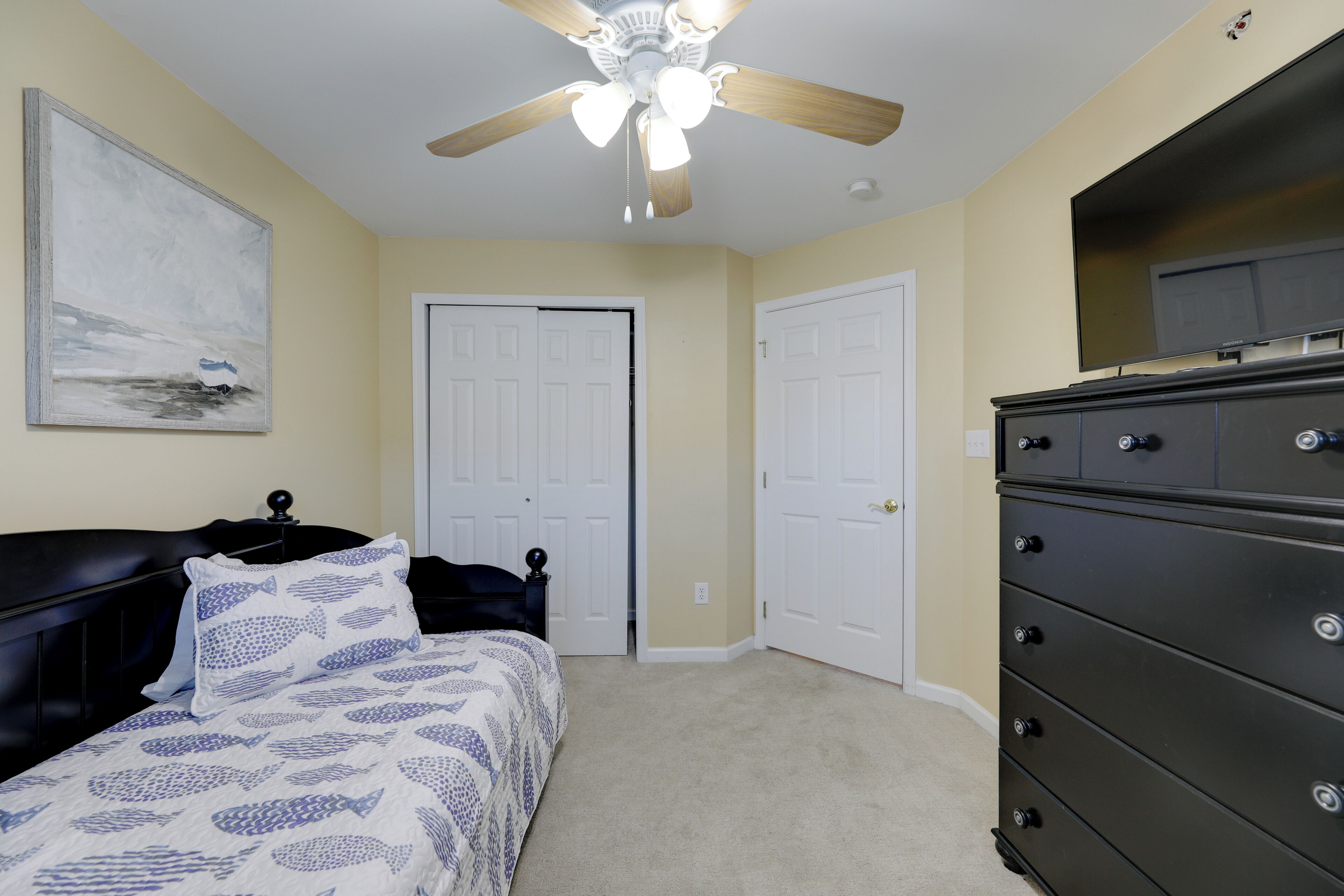 A bedroom with a bed, a dresser, a ceiling fan, and two doors.