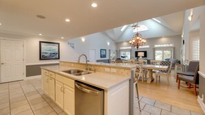 Un'ampia cucina con isola centrale, lavastoviglie integrata e zona pranzo illuminata da un lampadario.