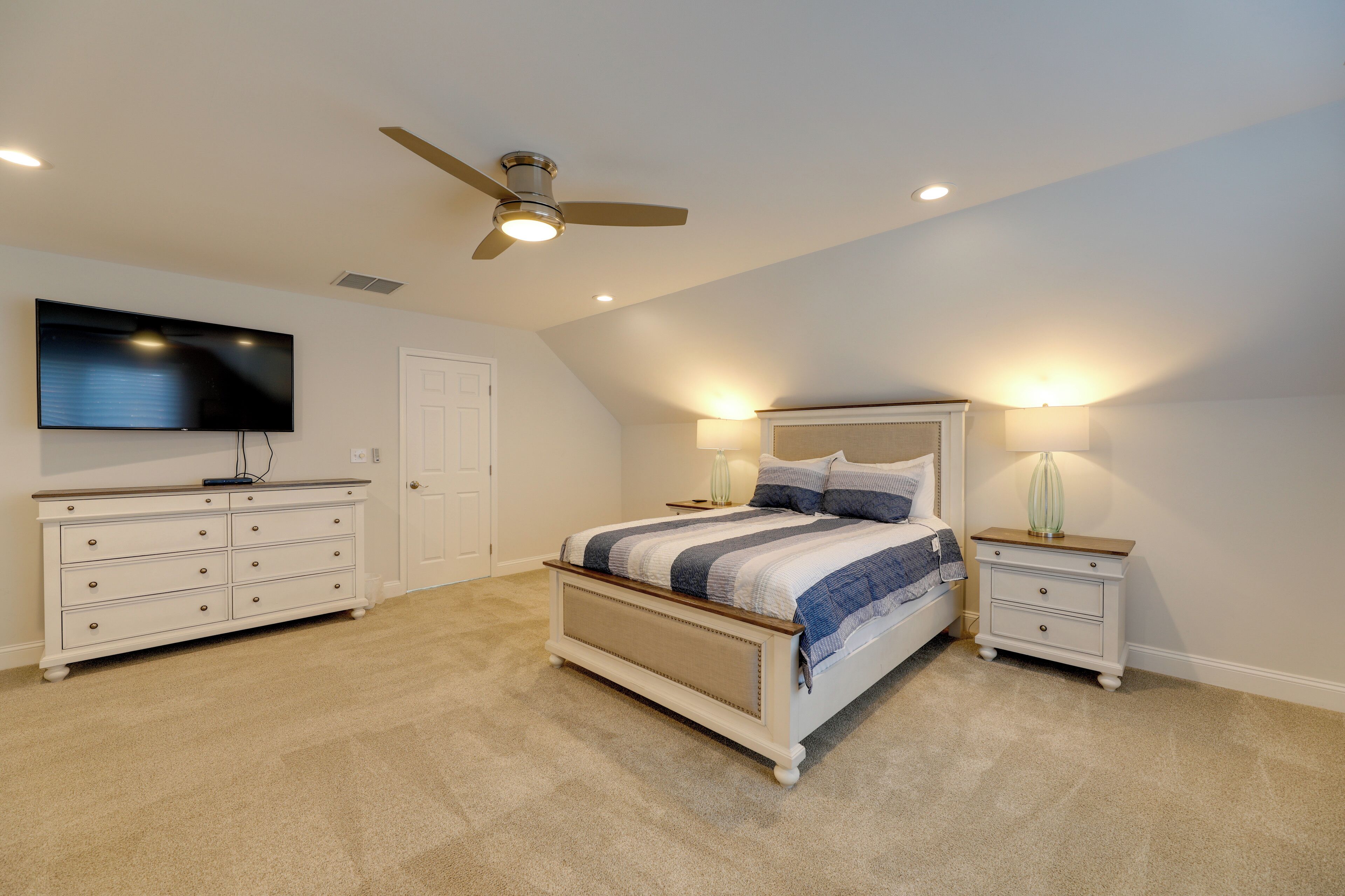 A bedroom with a bed, a dresser, a television, and a ceiling fan.