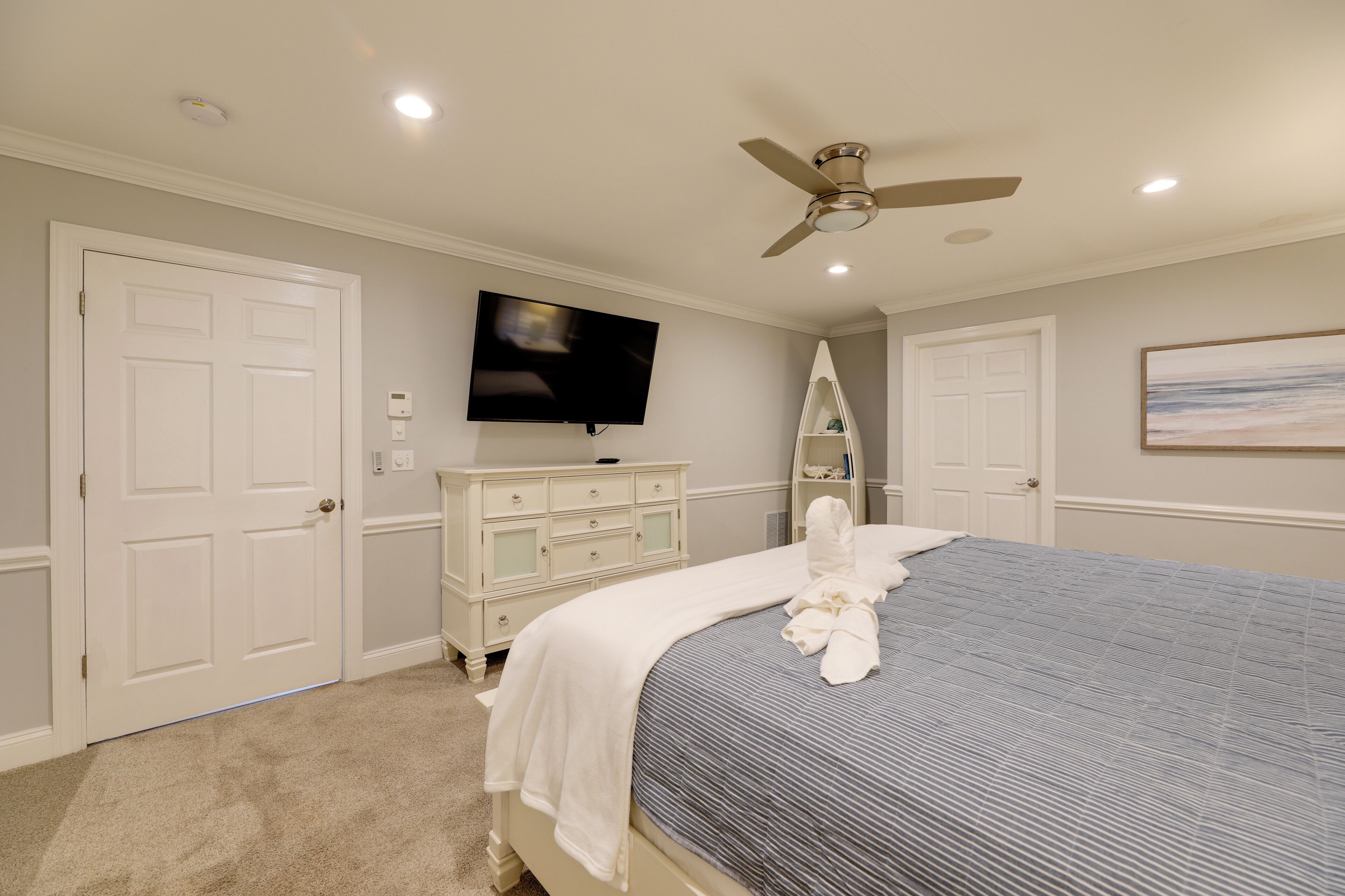 Un dormitorio con cama, ventilador de techo, televisor y cómoda.