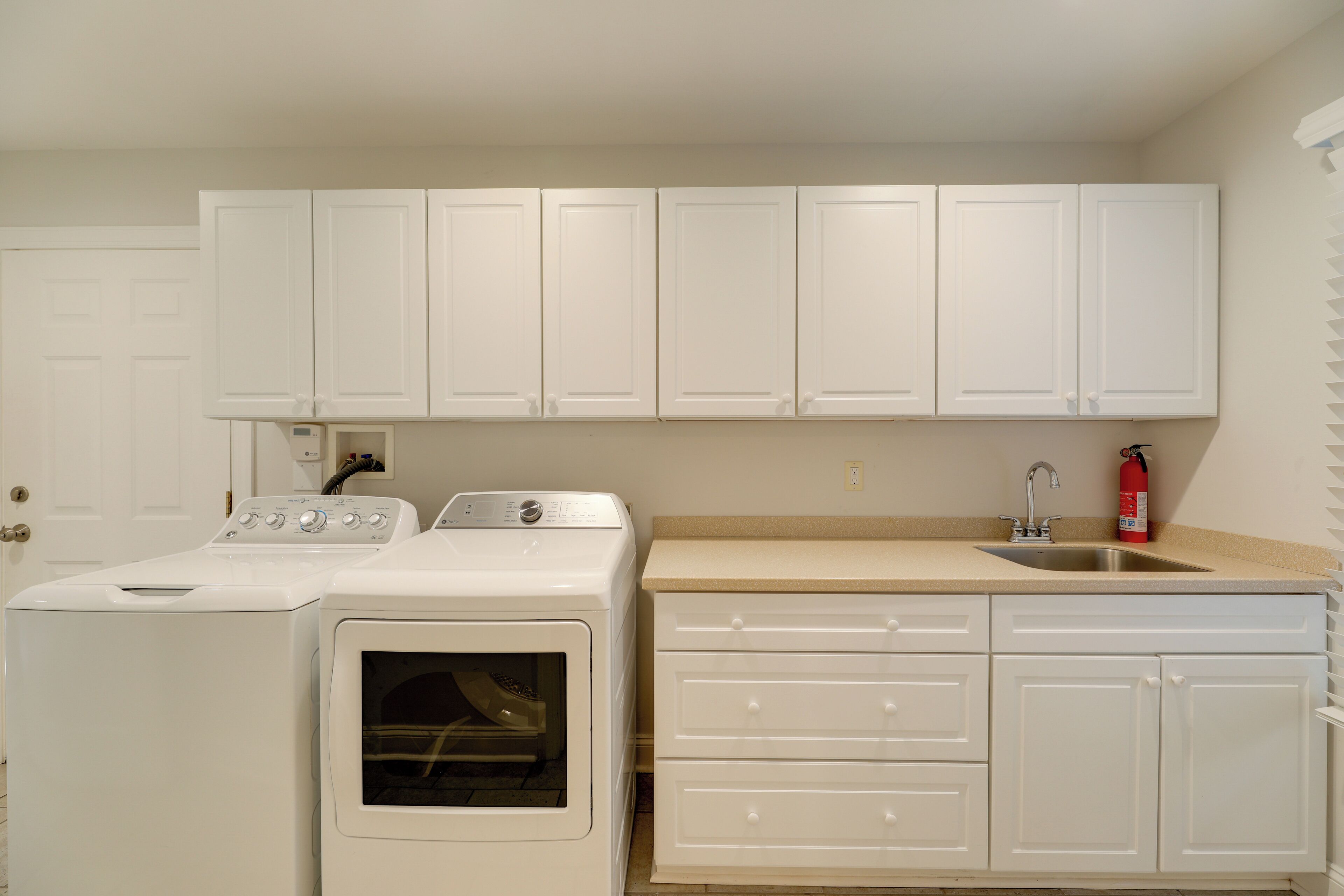 A laundry area with a washer and dryer, a sink, and white cabinets.