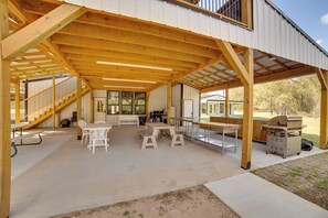 A covered outdoor patio with wooden beams, tables, chairs, and a grill.
