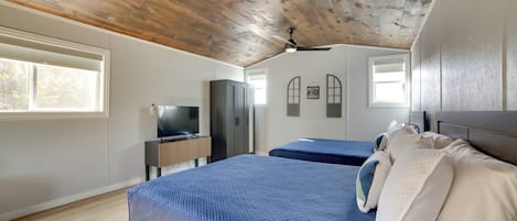 Un dormitorio con techo de madera, dos camas, un televisor y una ventana.