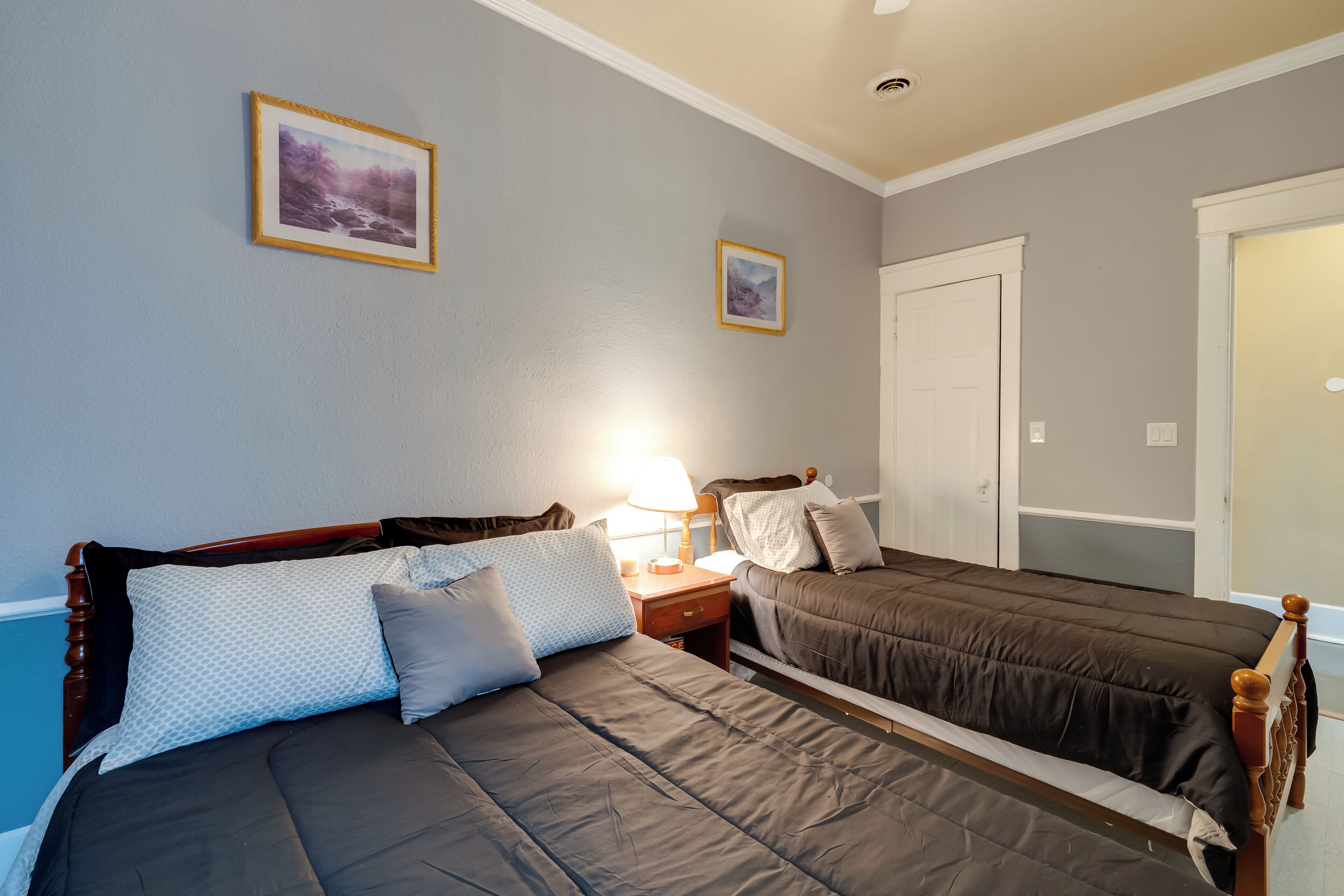 A bedroom with two beds, a nightstand, a lamp, and two framed pictures on the wall.