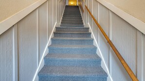 A staircase with a wooden handrail, carpeted steps, and white walls with a textured pattern. - Walkable Racine Retreat! 1 Mi to Lake Michigan (Racine)