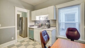 Una cocina compacta con armarios blancos, un refrigerador de acero inoxidable, un lavamanos y una ventana con persianas.
