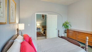 Un dormitorio con cama, cómoda, lámpara y puerta que da a otra habitación.