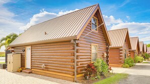 A row of log cabin-style buildings with a metal roof, a wooden door, and a small garden area with plants and flowers. - Unwind Poolside + Walk to Lake! Okeechobee Getaway (Okeechobee)