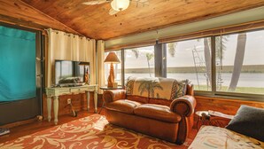 A cozy room with a leather sofa, a television, and a large window overlooking a body of water. - Unwind Poolside + Walk to Lake! Okeechobee Getaway (Okeechobee)