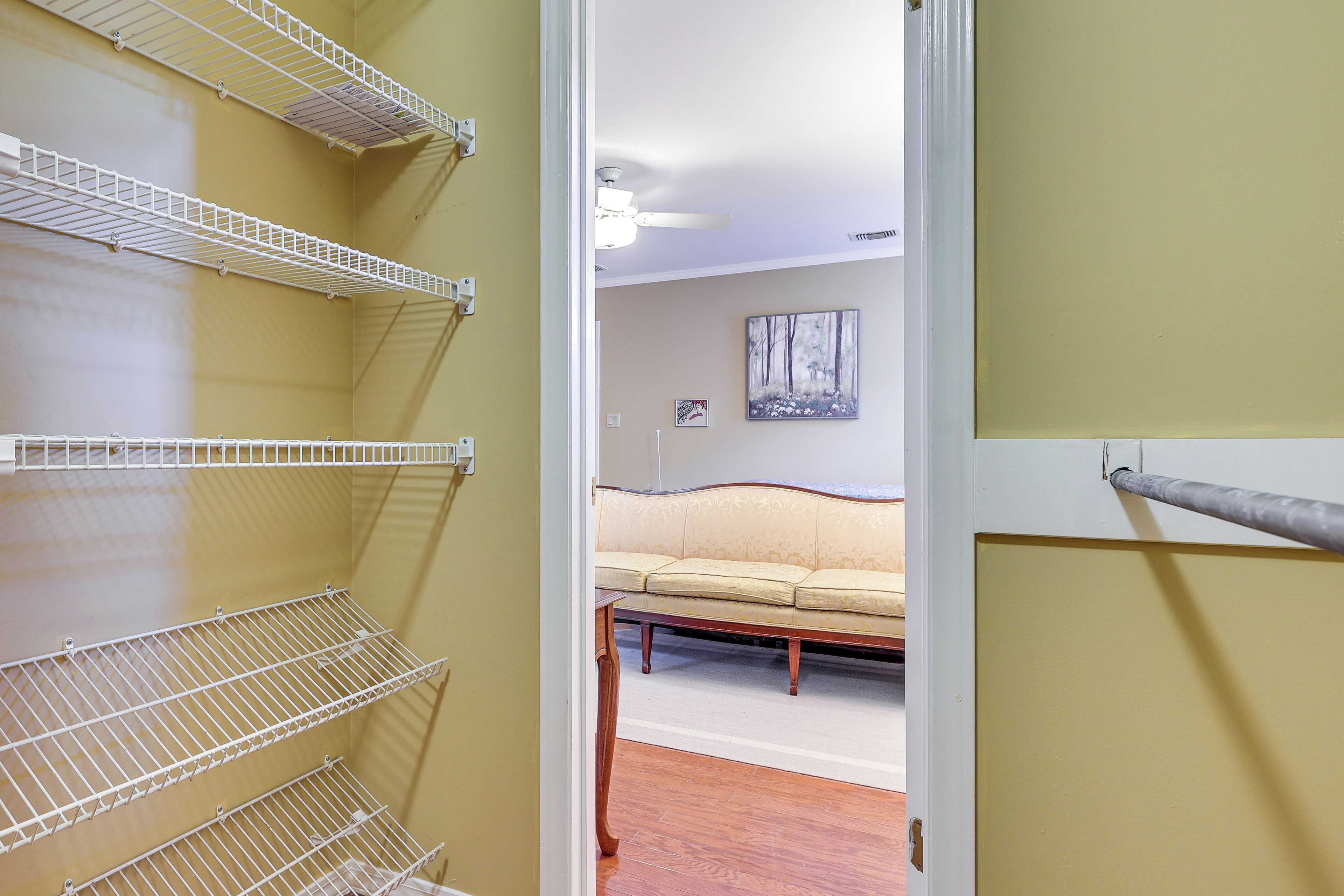 A room with a beige sofa, a wooden coffee table, and white wire shelves against a yellow wall.