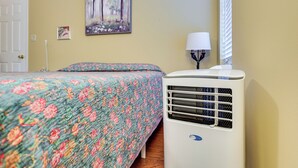A bedroom with a bed, a wall-mounted air conditioner, a lamp, and a door.