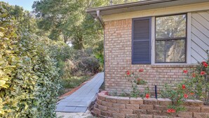 A house with a brick exterior, a window with shutters, and a brick flower bed with red flowers.