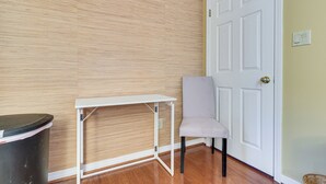 A room with a wooden wall, a white door, a trash bin, and a white table with a chair.