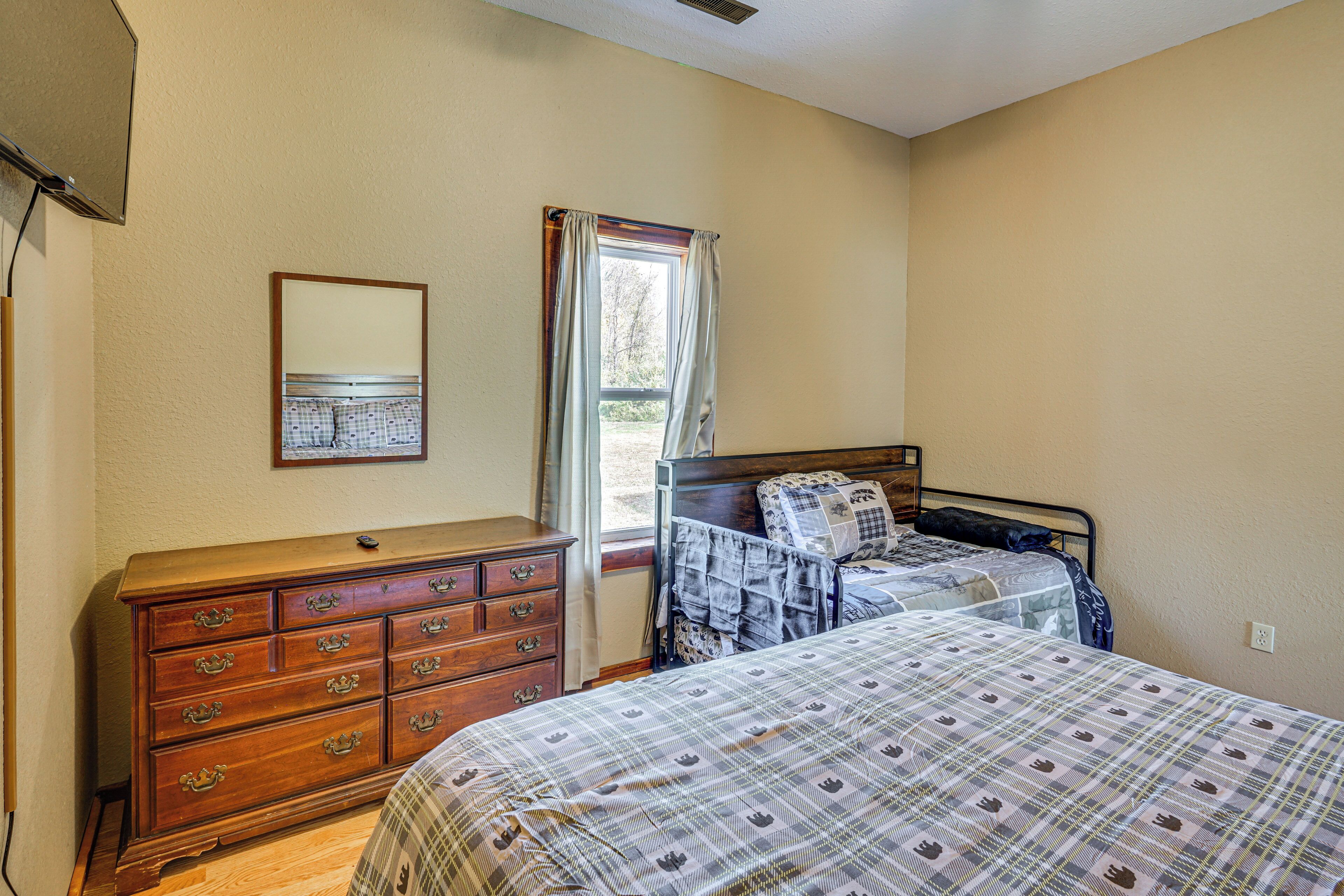 A bedroom with two beds, a wooden dresser, a mirror, and a window with curtains.
