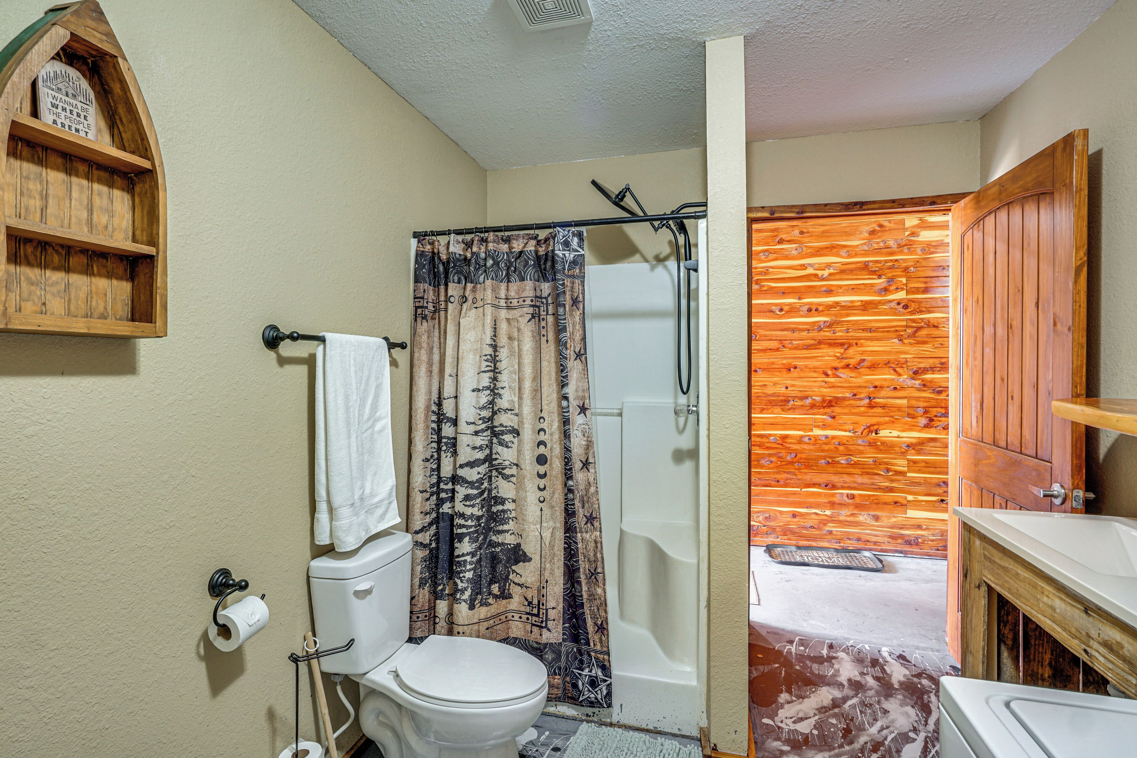 A bathroom with a toilet, shower curtain, wooden wall, and a wooden shelf with a sign.