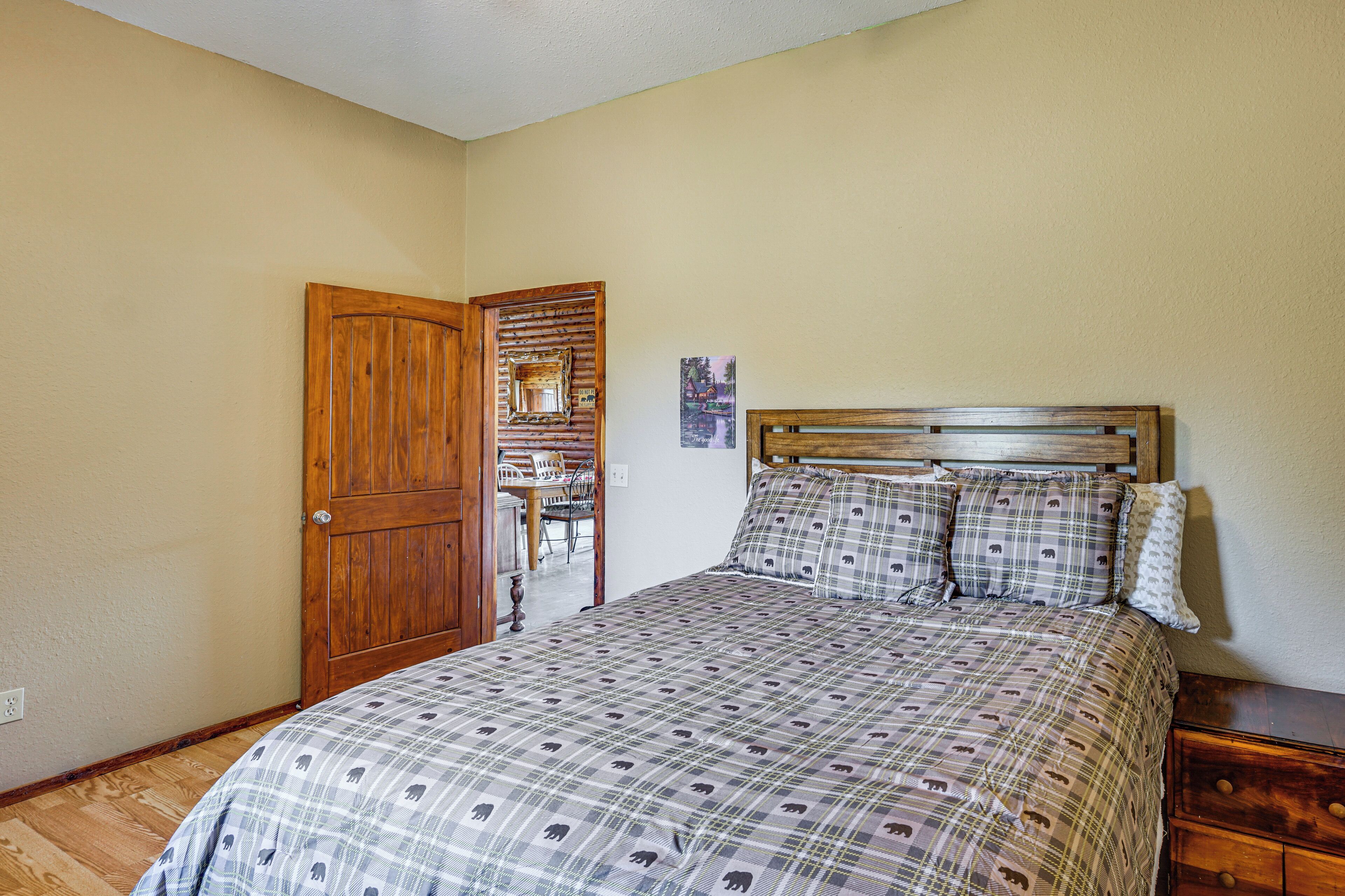 A bedroom with a wooden door, a bed with a patterned bedspread, and a small wooden nightstand.