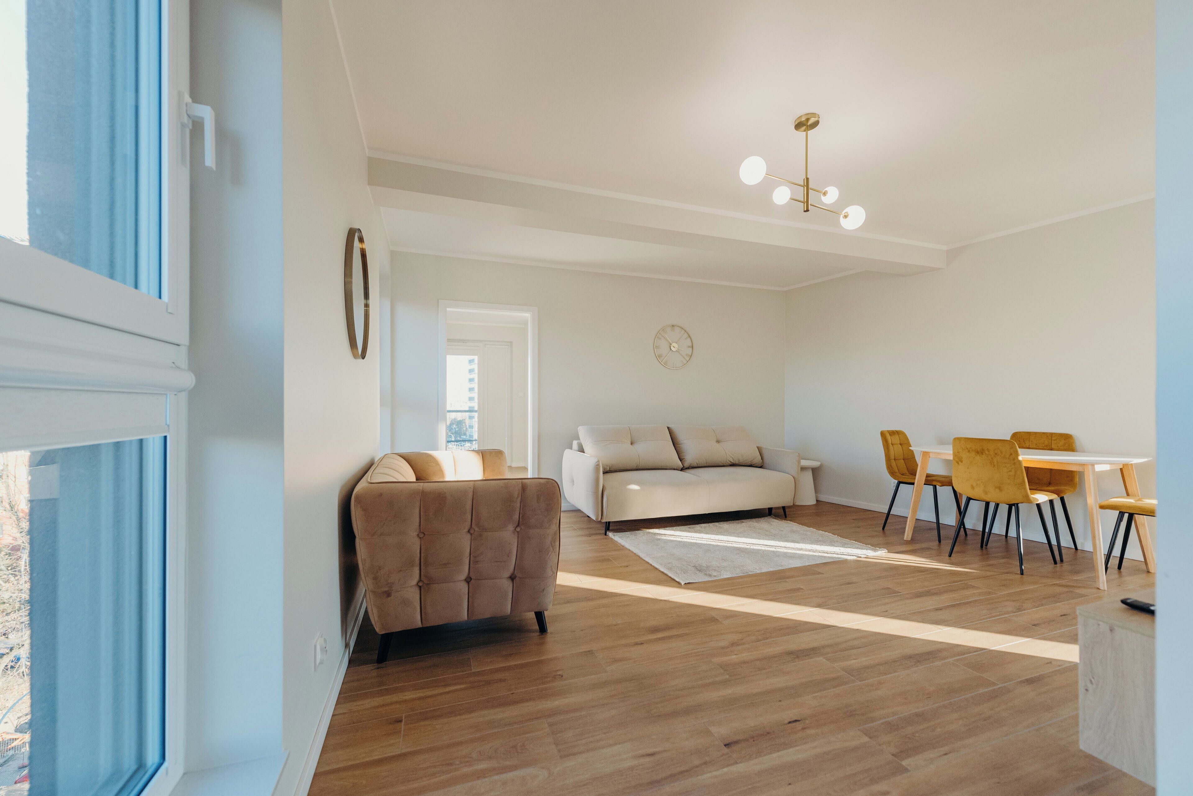 Amplia sala de estar con sofá, mesa de comedor con sillas, piso de madera y lámpara en el techo.