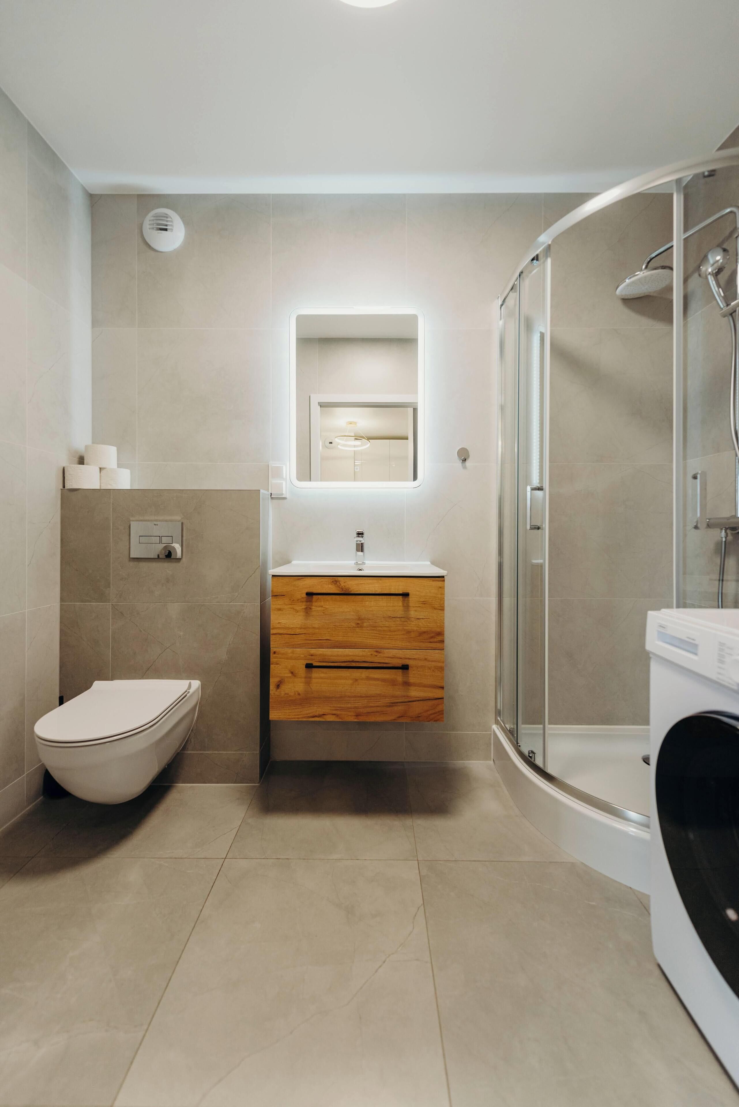 A modern bathroom with a toilet, wooden vanity, mirror, and glass shower enclosure.