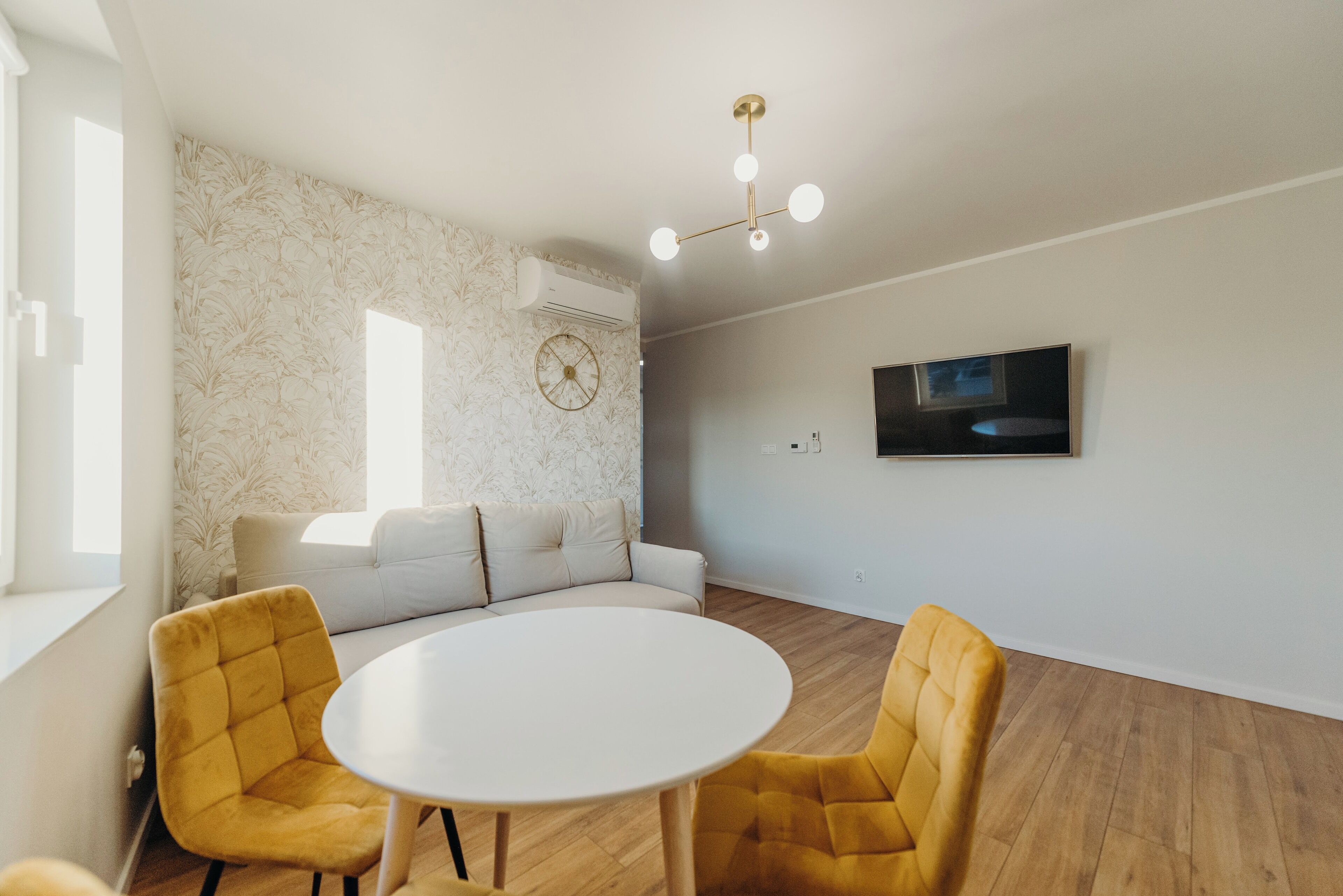 Uma sala de estar moderna com um sofá branco, poltronas amarelas, uma mesa redonda e um lustre no teto.