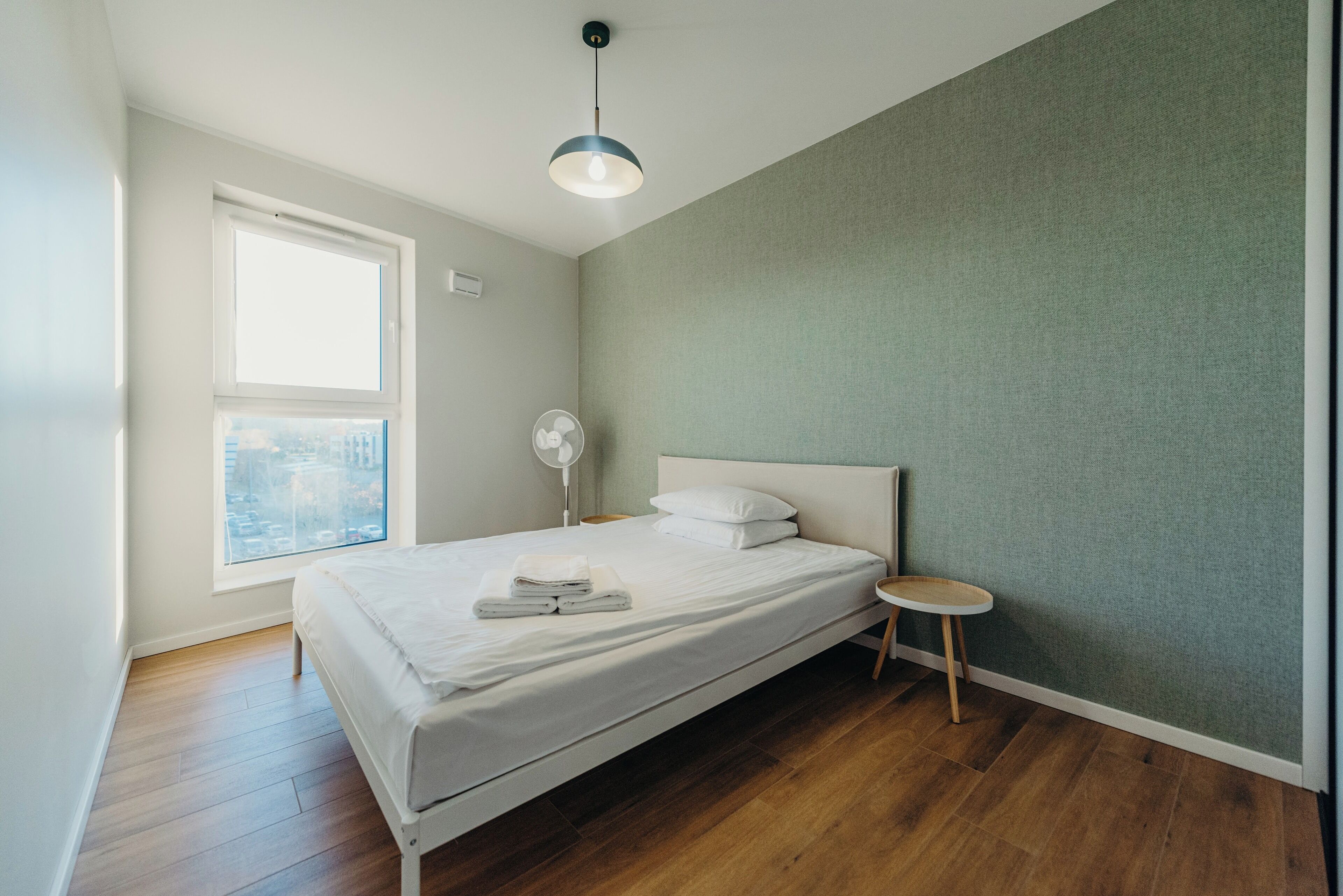 Un dormitorio con una cama, una mesita de noche, una ventana y una lámpara en el techo.