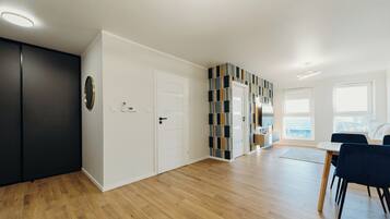 A modern living room with a wooden floor, a black wardrobe, a white door, and a dining area with a table and chairs.