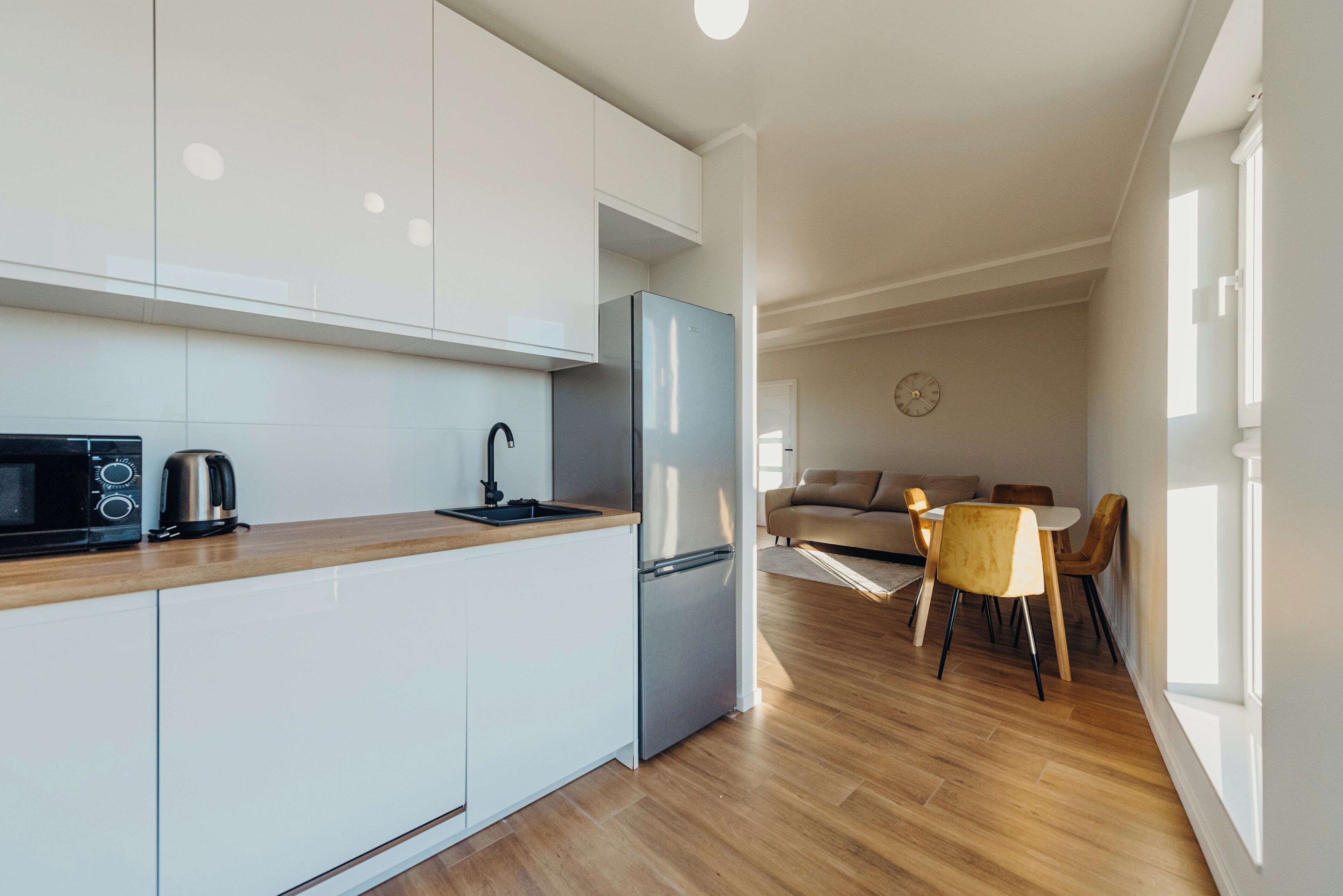 Una cocina moderna con armarios blancos, un refrigerador de acero inoxidable y un microondas. Hay un comedor con una mesa y sillas.