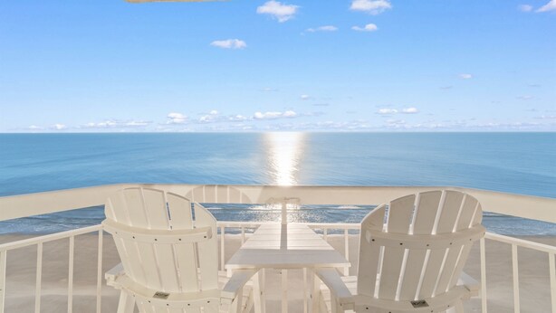 A balcony with two white Adirondack chairs and a small table, overlooking a calm sea and clear sky. - Rising Tides Properties Condo 1007 (Murrells Inlet)