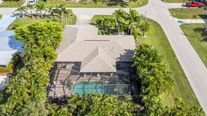 An aerial view of a residential property with a swimming pool, surrounded by lush greenery and palm trees.