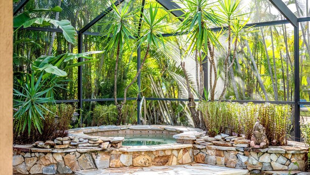 A hot tub surrounded by tropical plants and a stone wall.