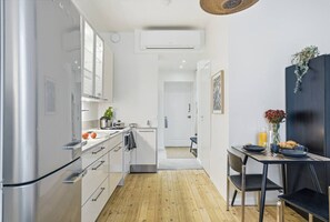 Eine moderne Küche mit Edelstahlgeräten, ein Essbereich mit Tisch und Stühlen sowie eine kleine Sitzecke mit einer Pflanze.