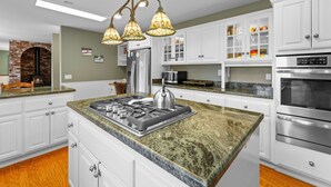 Eine moderne Küche mit weißen Schränken, einer Granit-Arbeitsplatte, einem eingebauten Herd und einem Backofen aus Ziegeln.