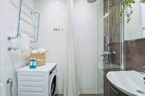Een moderne badkamer met een glazen douchecabine, een ingebouwde wasmachine en een wastafel met spiegel.