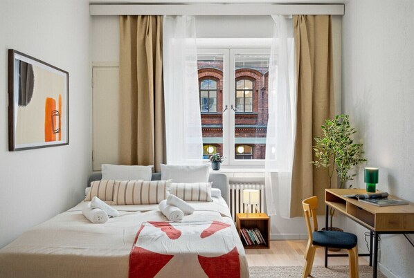 Een keurig opgemaakt hotelkamer met een bed, een bureau en een raam met gordijnen.