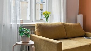 Et værelse med en sofa, et lille bord med en plante og et vindue med udsigt til bygninger.
