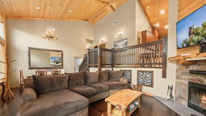 A cozy living room with a large sectional sofa, a wooden coffee table, a fireplace, and a staircase leading to an upper level. - Bear State of Mind - Close to Ski Slopes, Hot Tub, Foosball, Fireplace, Deck, BBQ (Big Bear City)