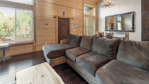 A log cabin interior with a sectional sofa, a dining table with chairs, a wooden bench, and a large mirror on the wall. - Bear State of Mind - Close to Ski Slopes, Hot Tub, Foosball, Fireplace, Deck, BBQ (Big Bear City)