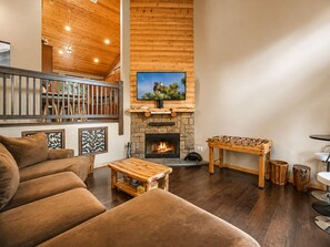 A cozy living room with a fireplace, a television mounted on a wooden wall, and a foosball table. - Bear State of Mind - Close to Ski Slopes, Hot Tub, Foosball, Fireplace, Deck, BBQ (Big Bear City)