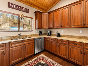 A kitchen with wooden cabinets, a stainless steel dishwasher, and a coffee maker. - Bear State of Mind - Close to Ski Slopes, Hot Tub, Foosball, Fireplace, Deck, BBQ (Big Bear City)