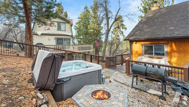 A hot tub, a fire pit, and a barbecue grill in a backyard with a wooden deck and a house in the background. - Bear State of Mind - Close to Ski Slopes, Hot Tub, Foosball, Fireplace, Deck, BBQ (Big Bear City)