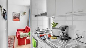 Una cocina moderna con armarios blancos, un sofá rojo y una cafetera.